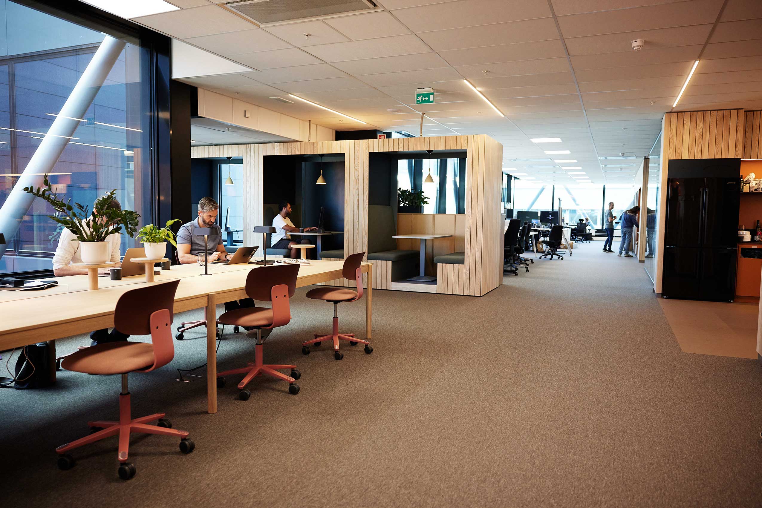 Neat's office space with red HAG tion chairs at a desk and booth seating behind