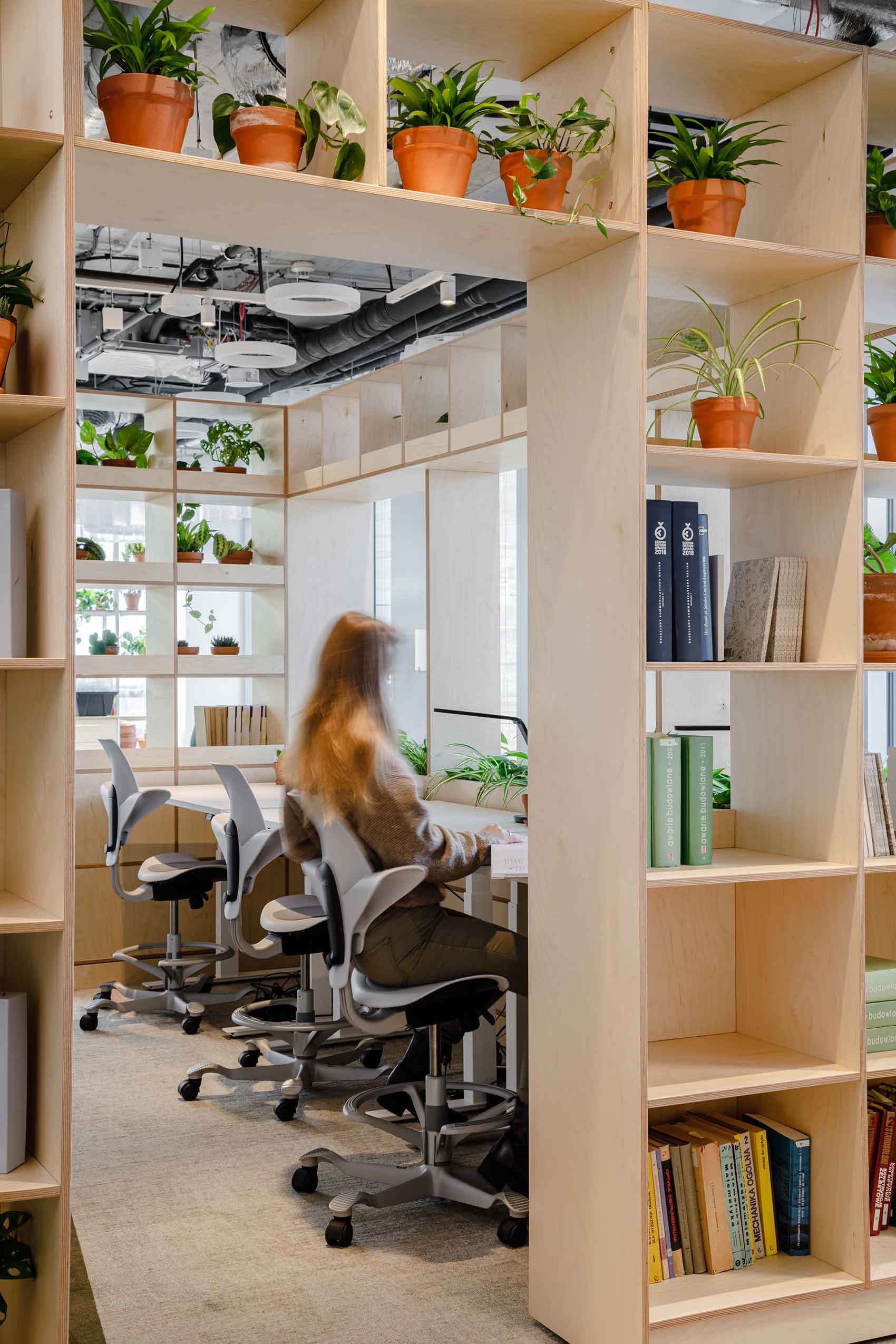 a lady sat working a HÅG Capisco chair in Arup's new office, with wooden shelving units.