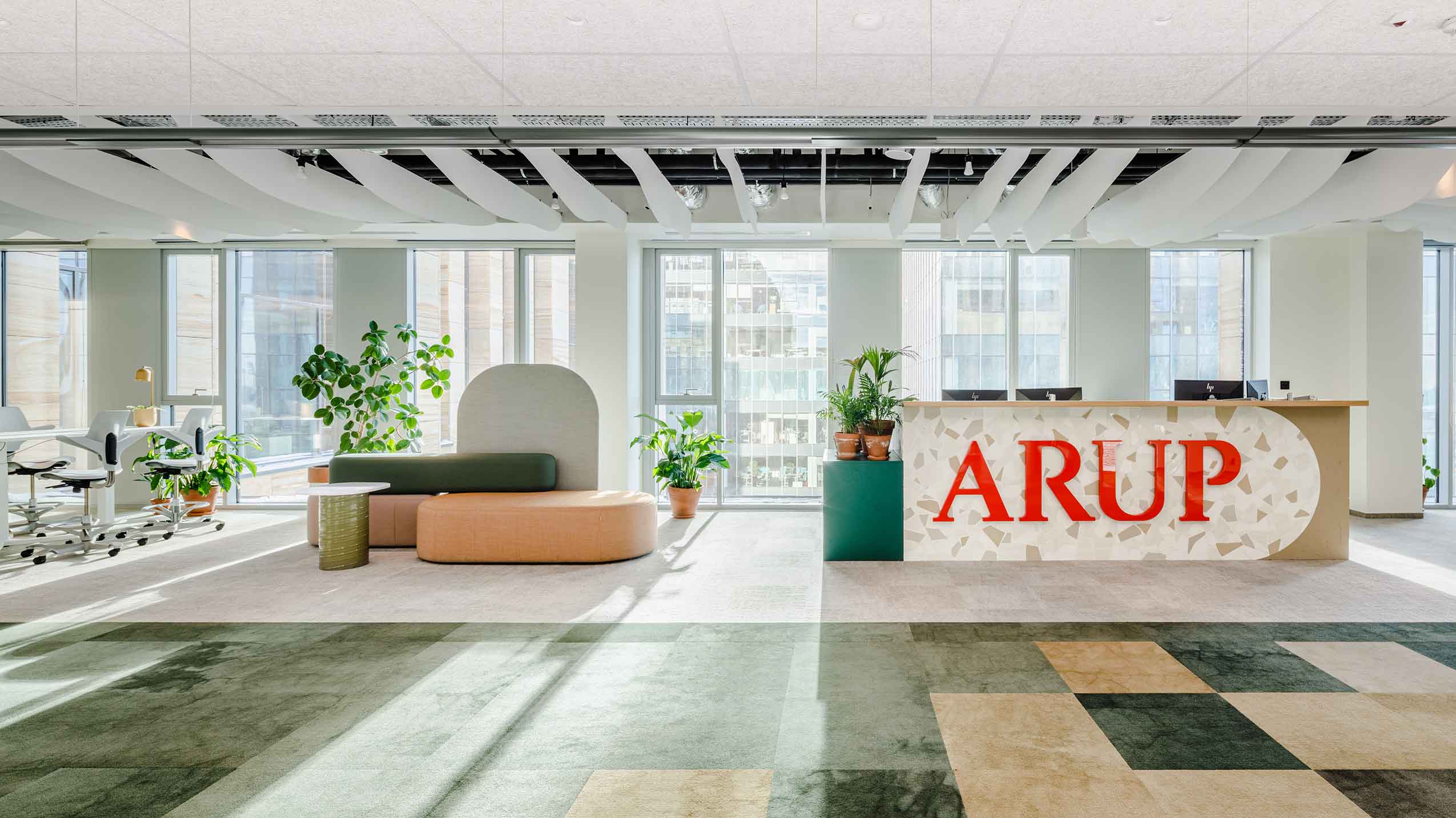 Angle 2 of The Foyer in Arup's new office, with their bran dname on the reception desk and open space including seating.