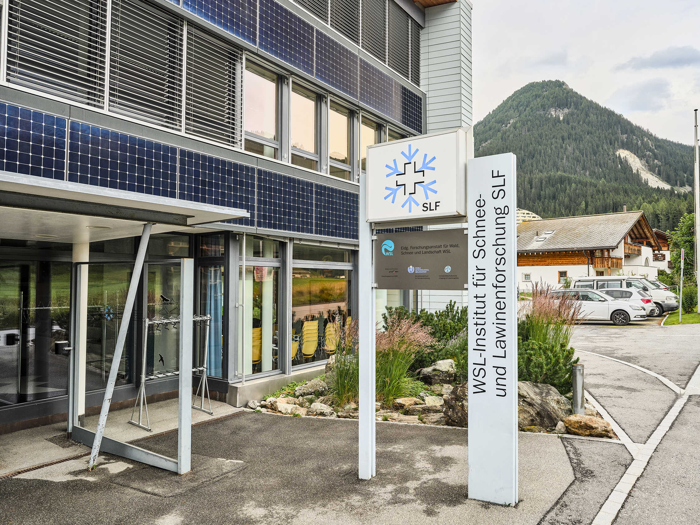 Exterior image of Swiss avalance centre, a glass and steel office building with steel supports and a sign out front