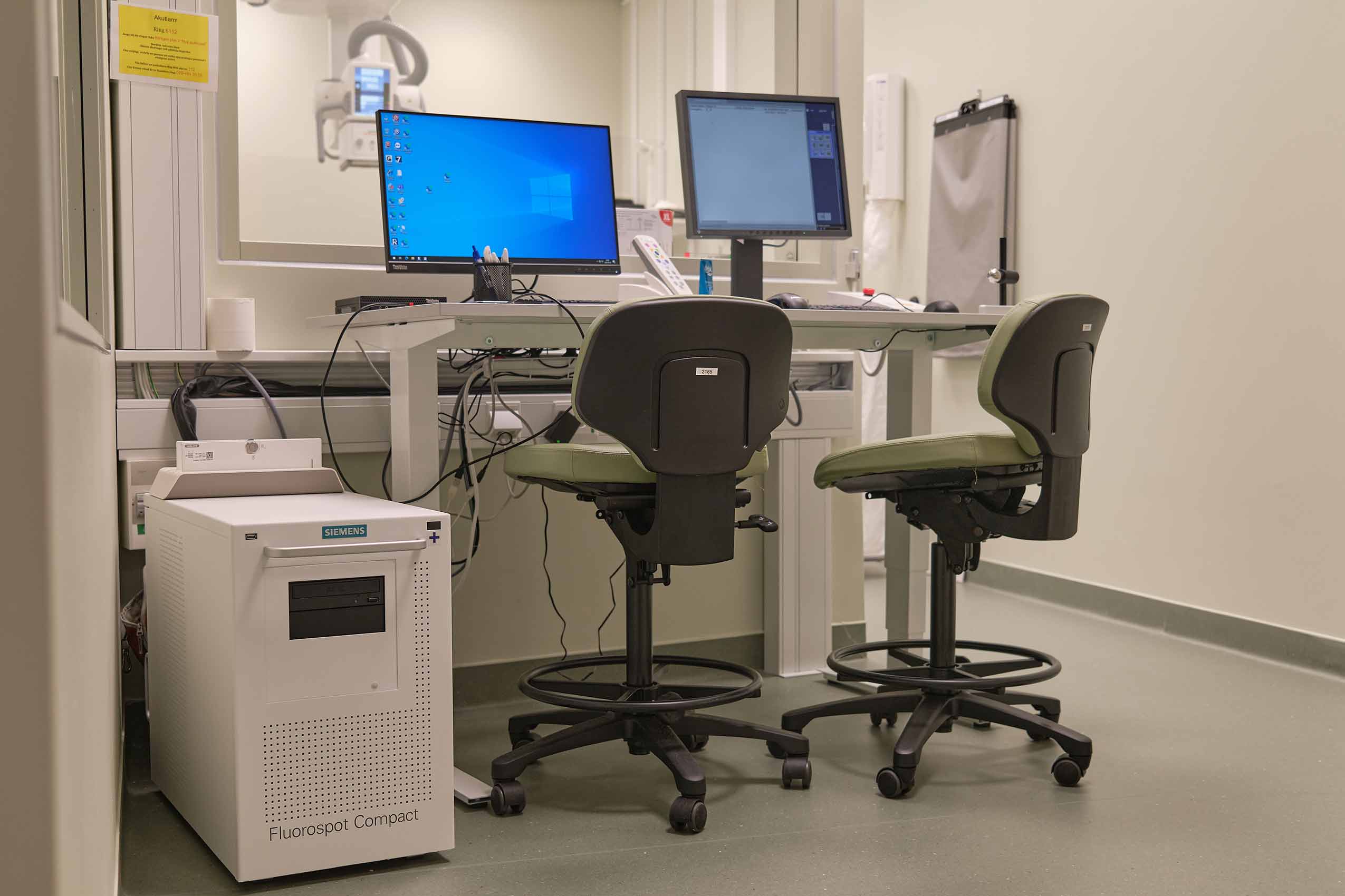 2 RH Activ chairs in green behind 2 meidcal monitoring computer screens on a table, in a white room