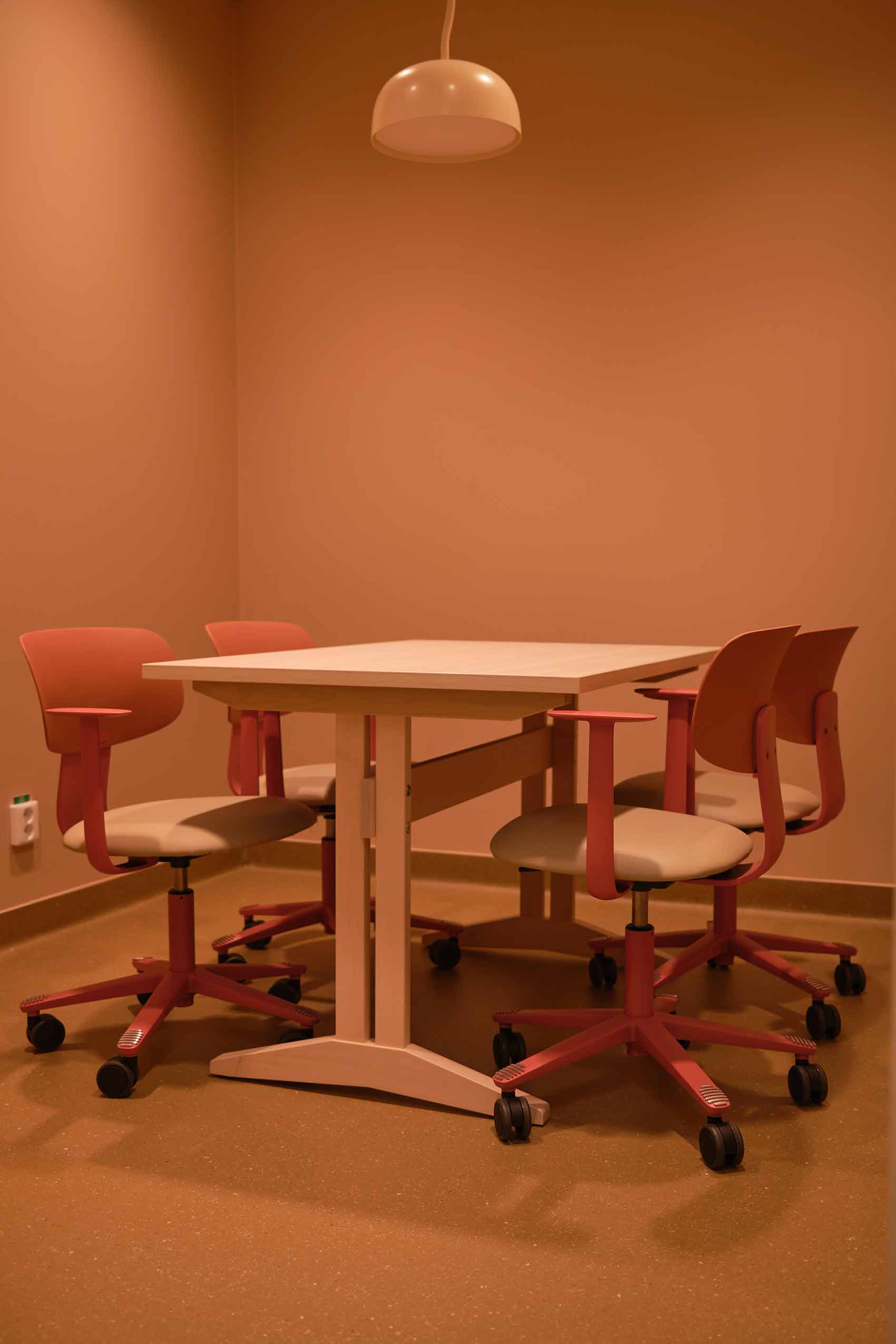 Ersta hospital meeting table with plain beige walls, and 4 HÅG Tion chairs in rose around a table with a ceiling light visible at the top of the picture