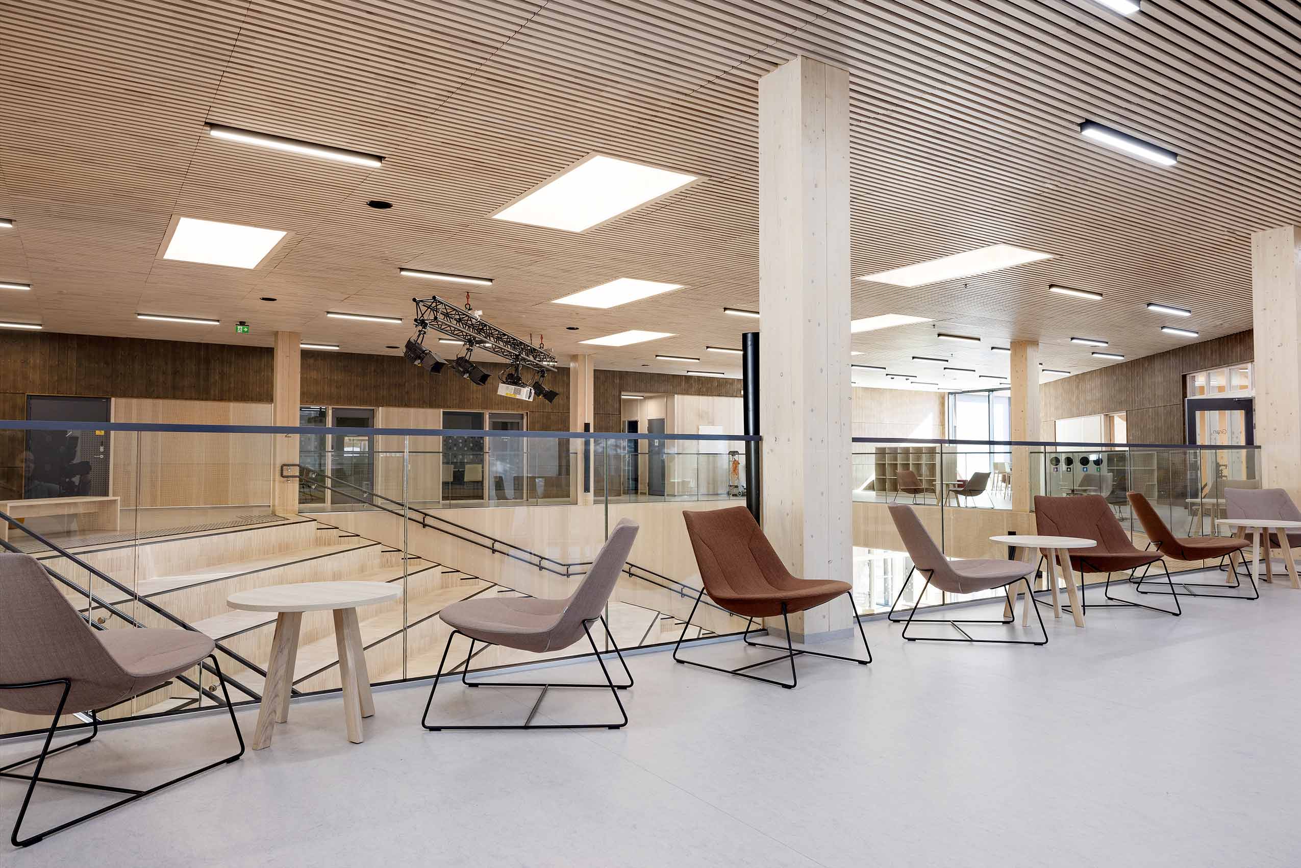 Several Profim Chic chairs facing the camera with a small table between them, on a second floor walkway at a school, with a glass panel overlooking the first floor, and wooden clad walls and beams