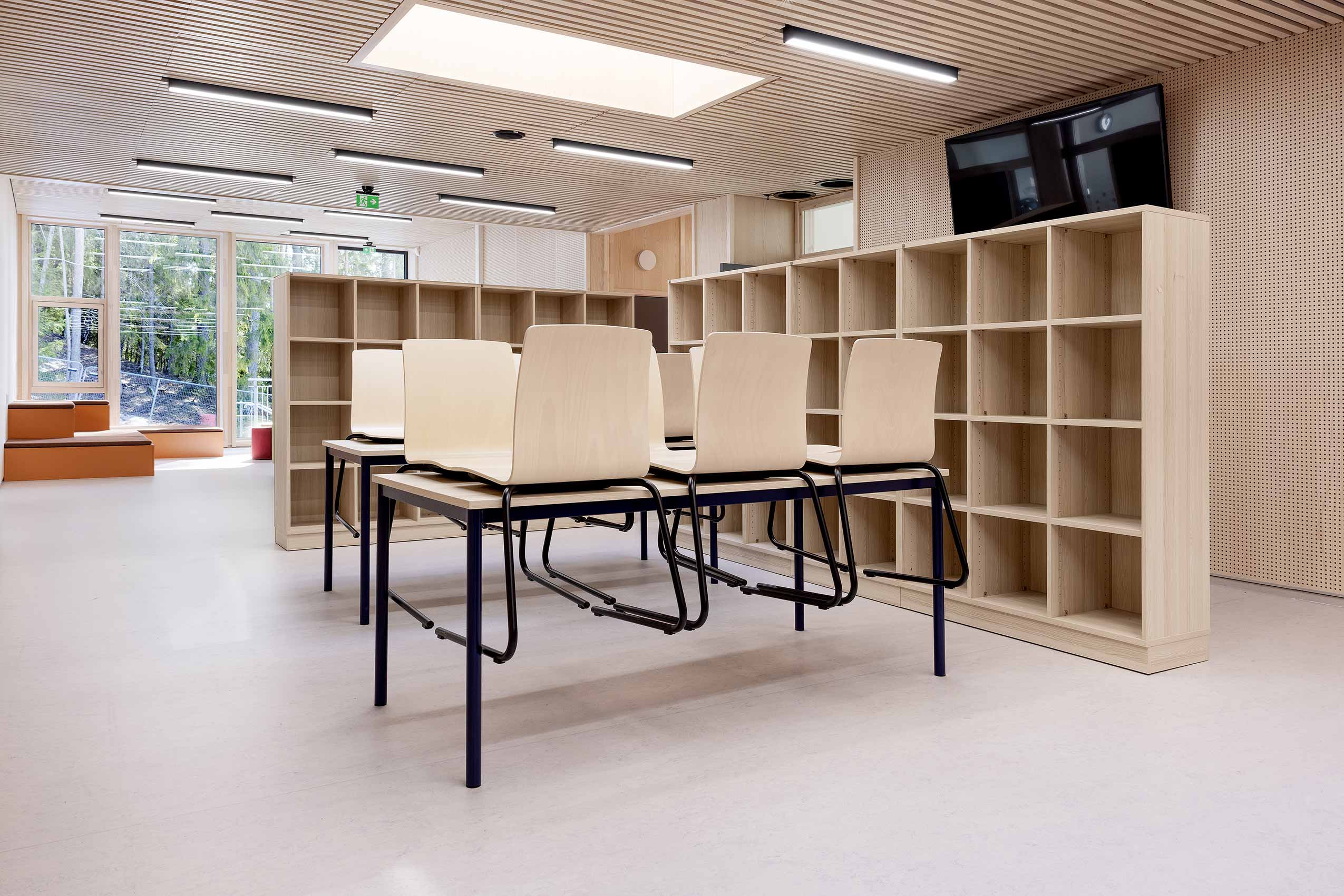 School room at HOV school, with multiple Profim com chairs in wood placed ontop of tables ready for cleaning, and a wooden open cupboard along the wall in the background