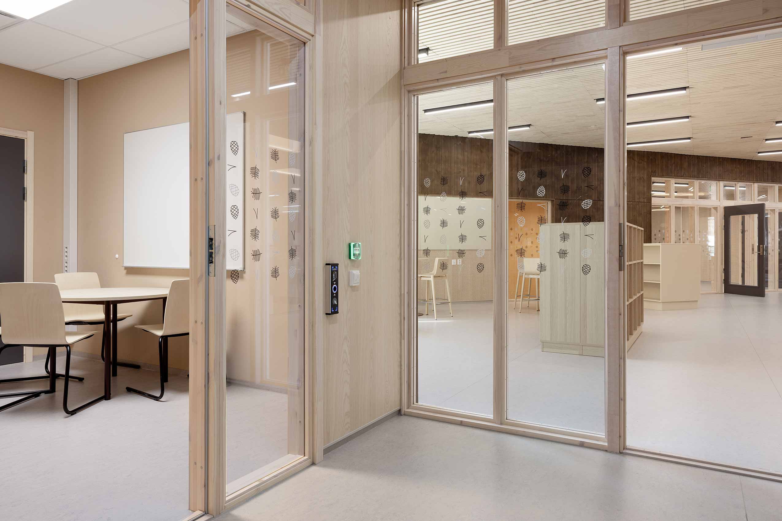 Inside HOV school, with Profim Com chairs around a tabel on the left, and glass door and wall ont he right showing a view into another room. all walls are either glass or wooden