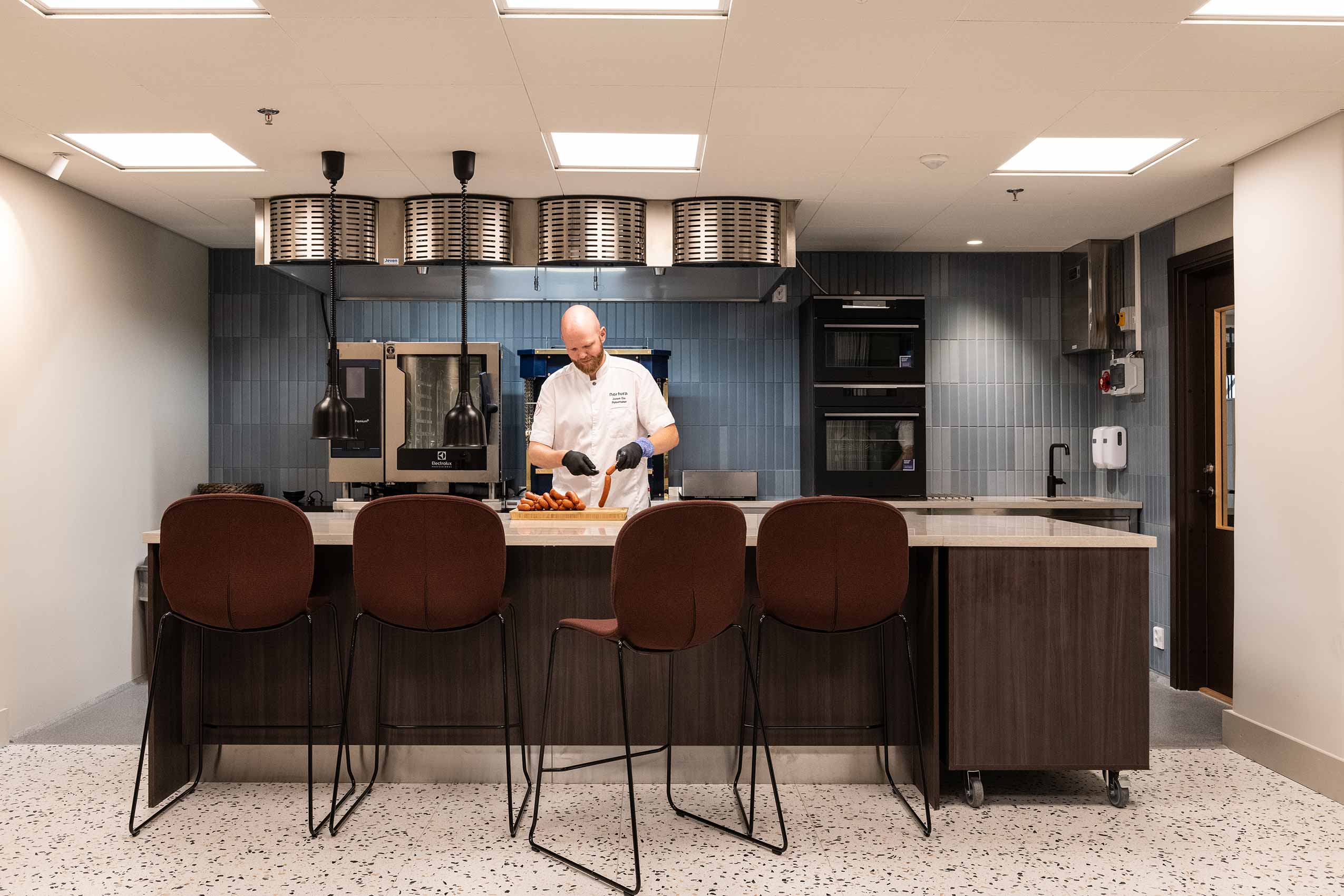 4 red Profim Noor chairs lined up behind a kitchen surface with a chef cooking as if for a demonstration
