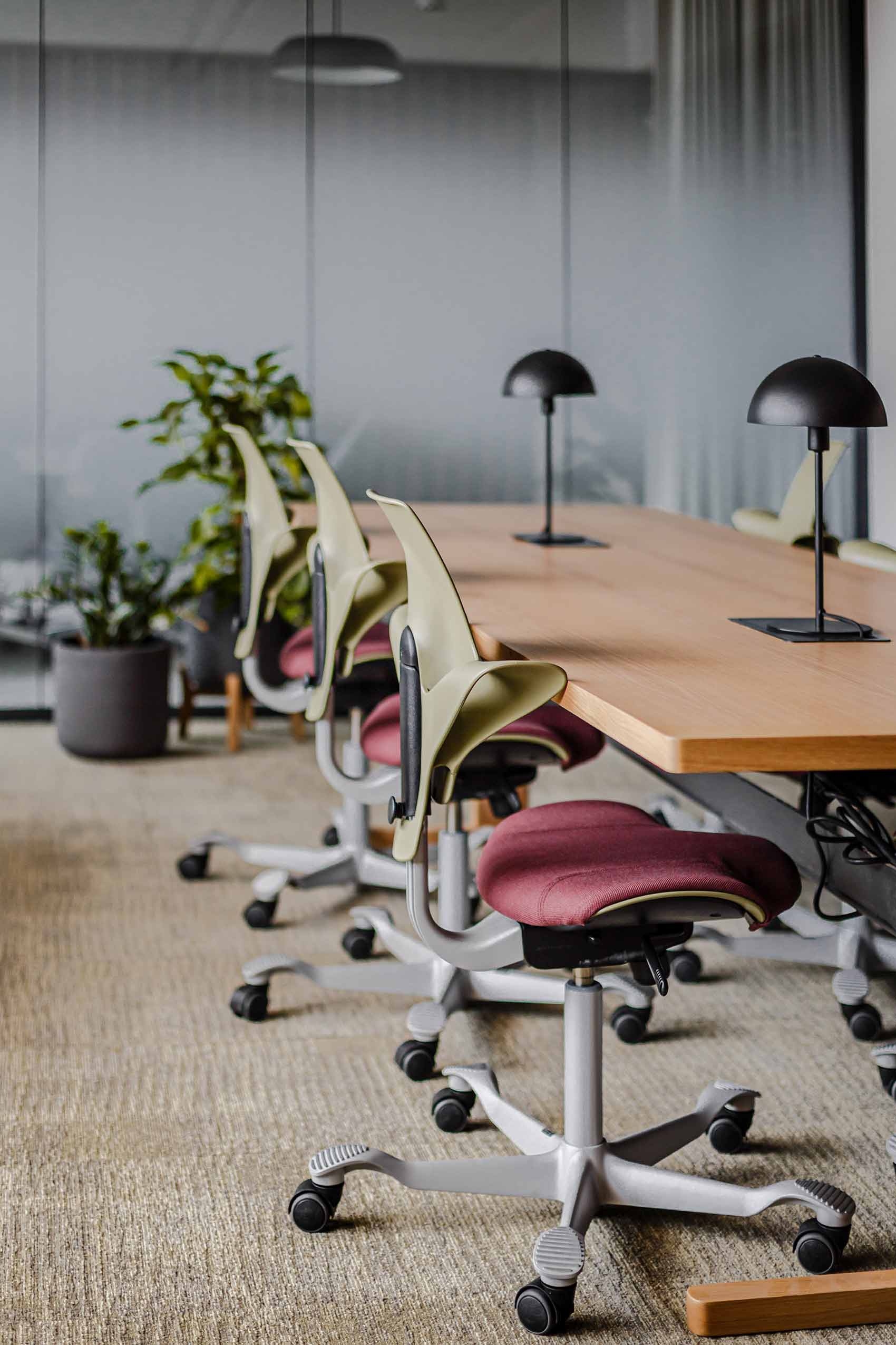 a bank of HÅG Capisco Puls chairs in green plastic, along a wooden table in an office