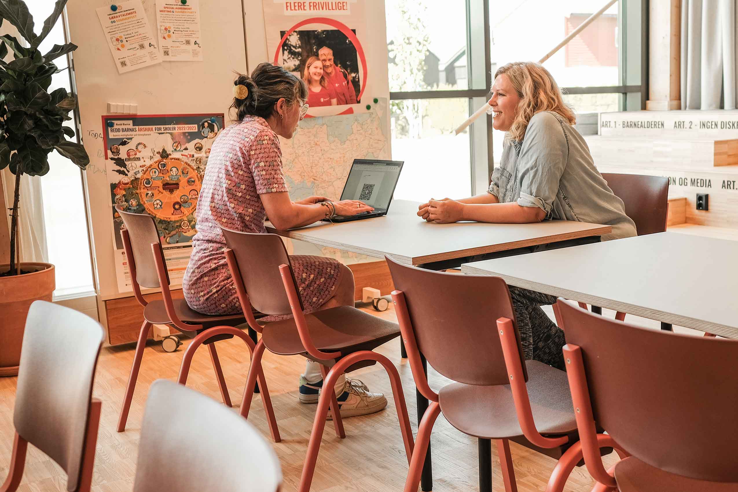 Two people talking sat no brick red HÅG celi chairs at a table, in Redd Barna's Oslo office