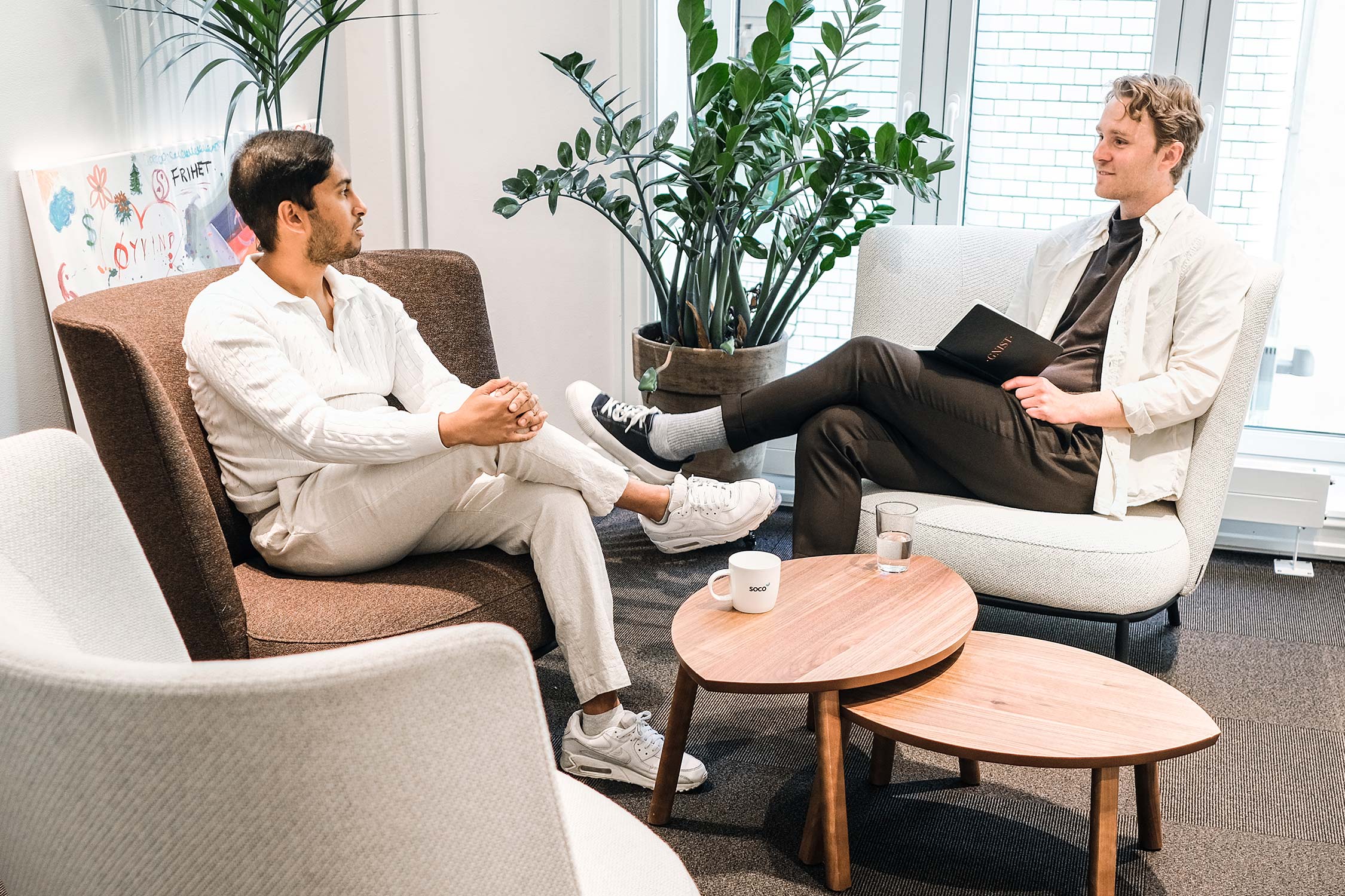 Two people talking relaxing in Offecct Shift chairs, with Offecct Phoenix tables in front of them