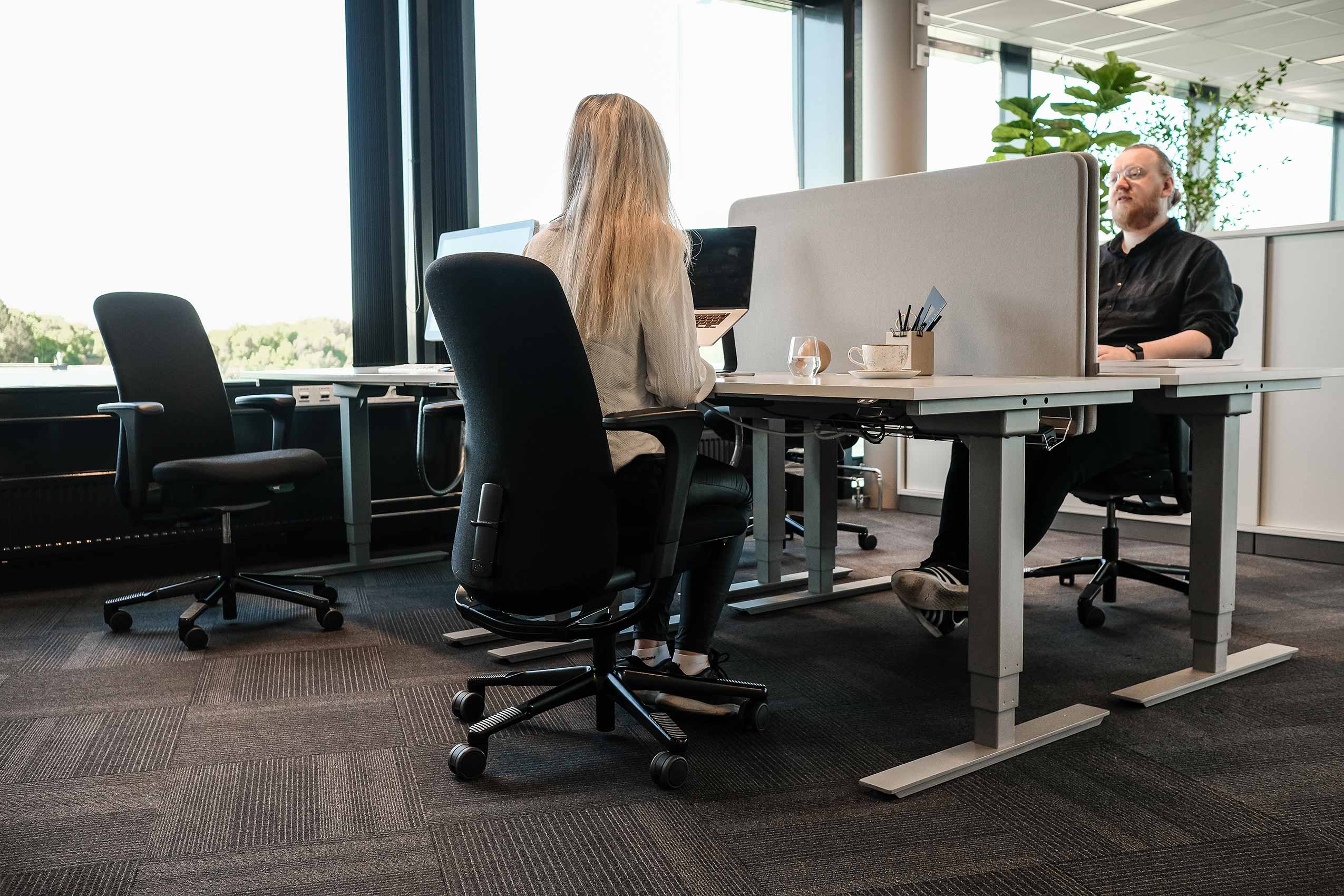 Two people sat in HÅG Sofi chairs opposite each other at workstatiosn in Strex's Oslo office
