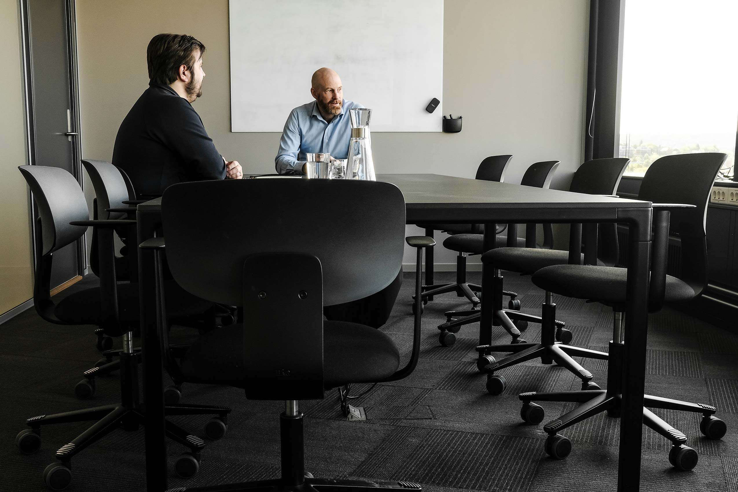 Angle 2 of two people sat in black HÅG Tion chairs around a meeting table at Strex's new office