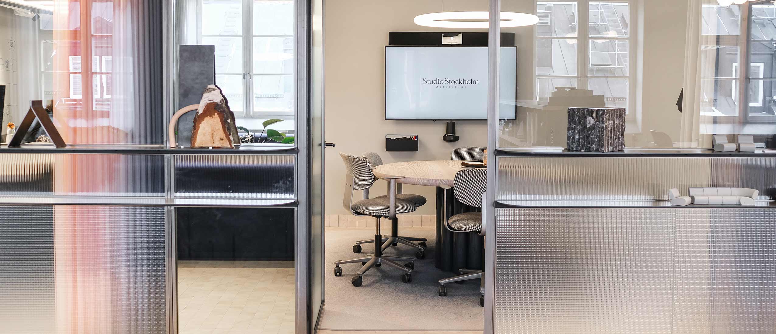 looking into a meeting room through windowed walls, HÅG Tion chairs are around a table and a TV screen is up on the wall.