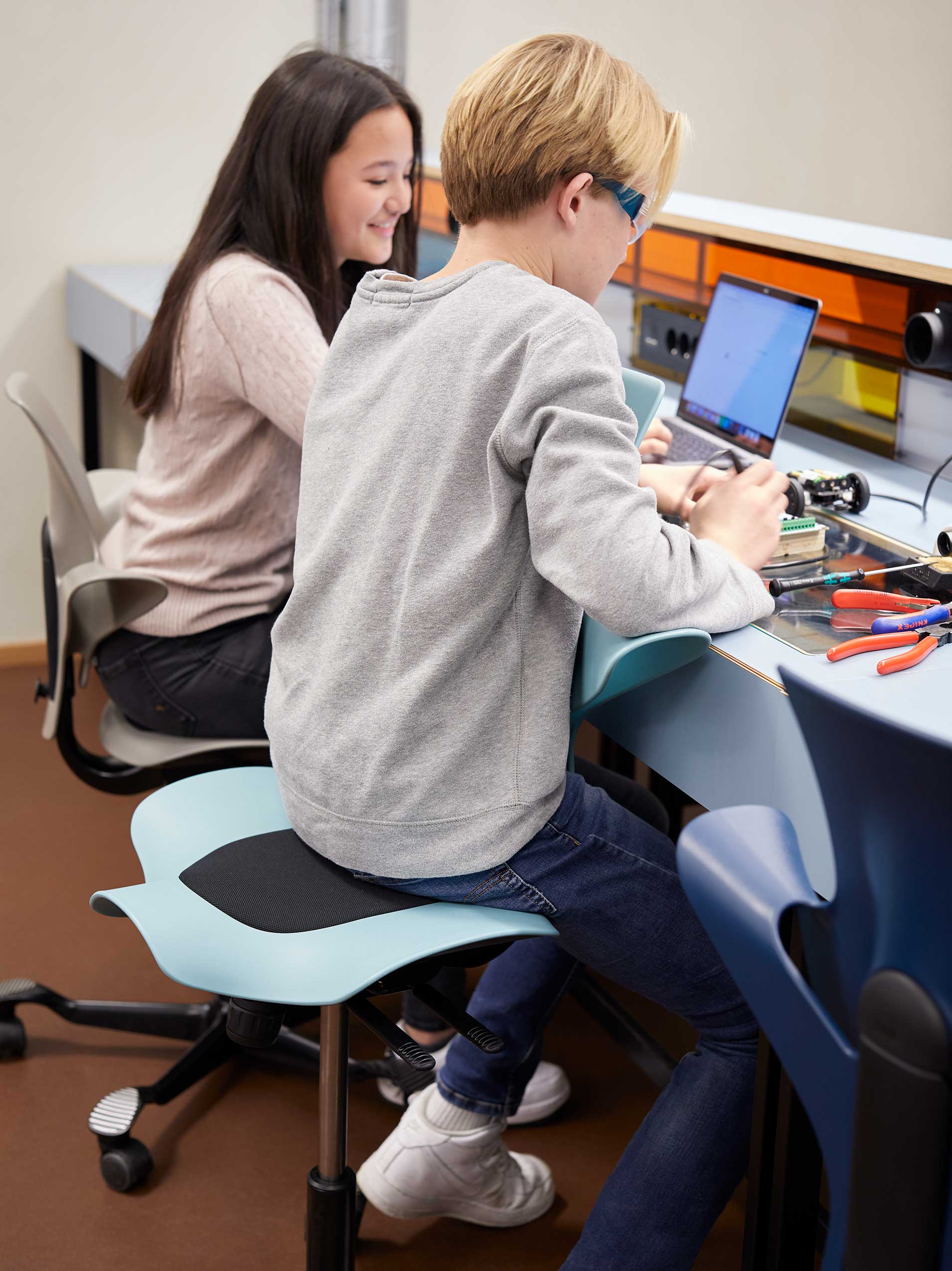 2 teenagers sitting in colourful HÅG Capisco Puls chairs in the Teknolab workshop in Oslo