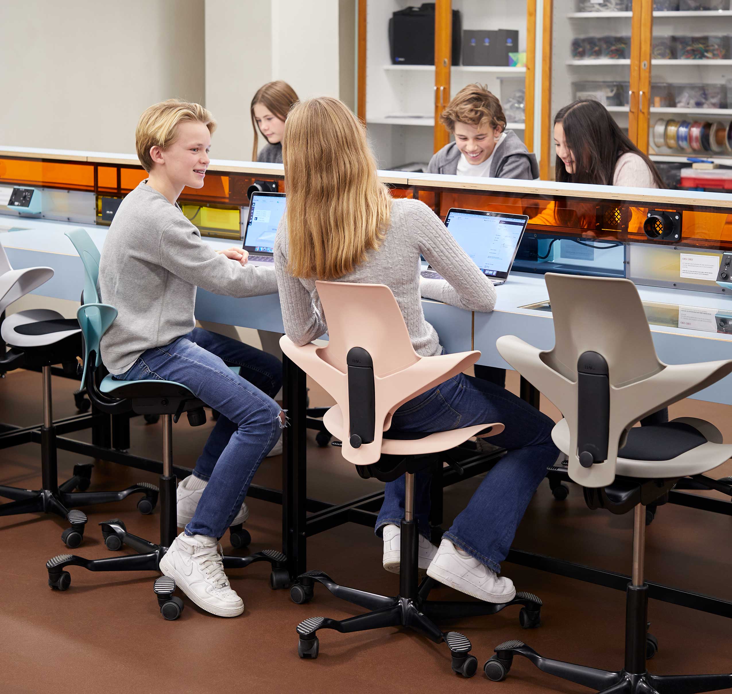 2 teenagers sitting in colourful HÅG Capisco Puls chairs in the Teknolab workshop in Oslo