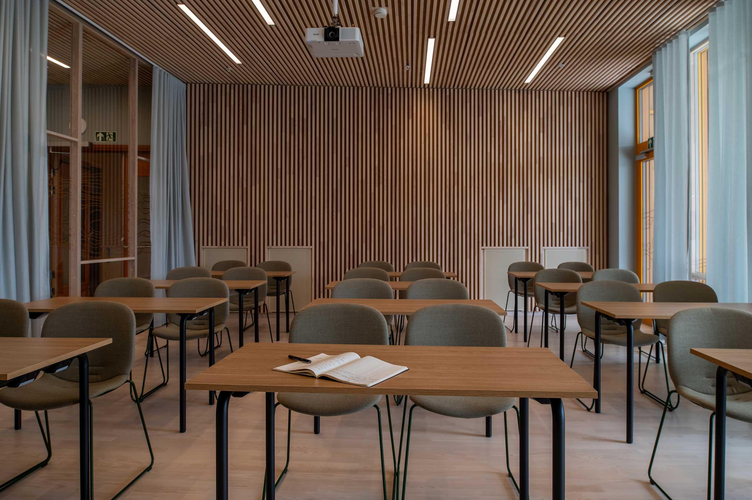 3 rows of rectangle tables with wooden surfaces and 2 Profim Noor chairs behind each table. the walls are wooden paneling