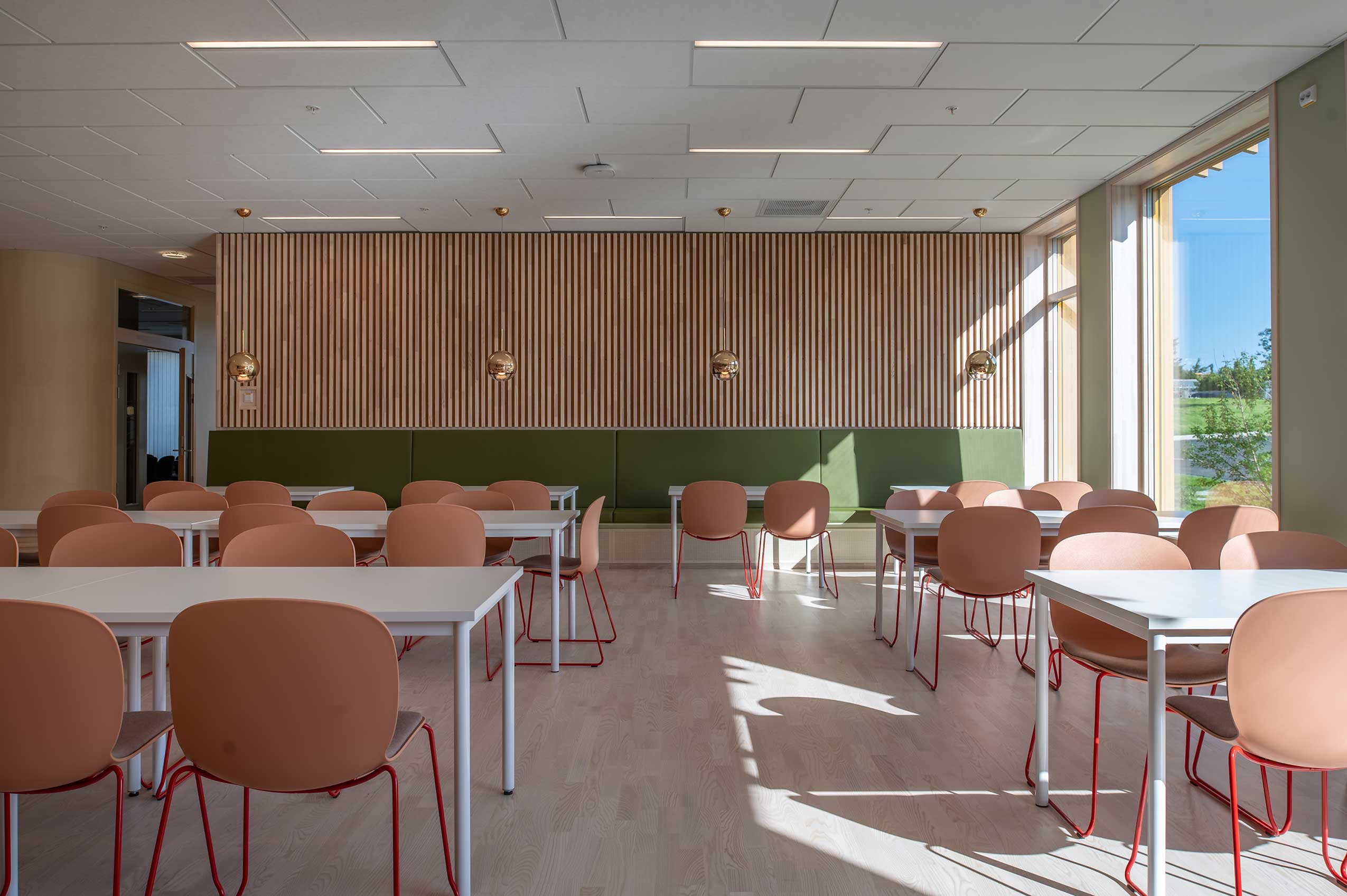 interior of dining room area with wooden panel walls and a green lower part, with coral Profim Noor chairs around tables 