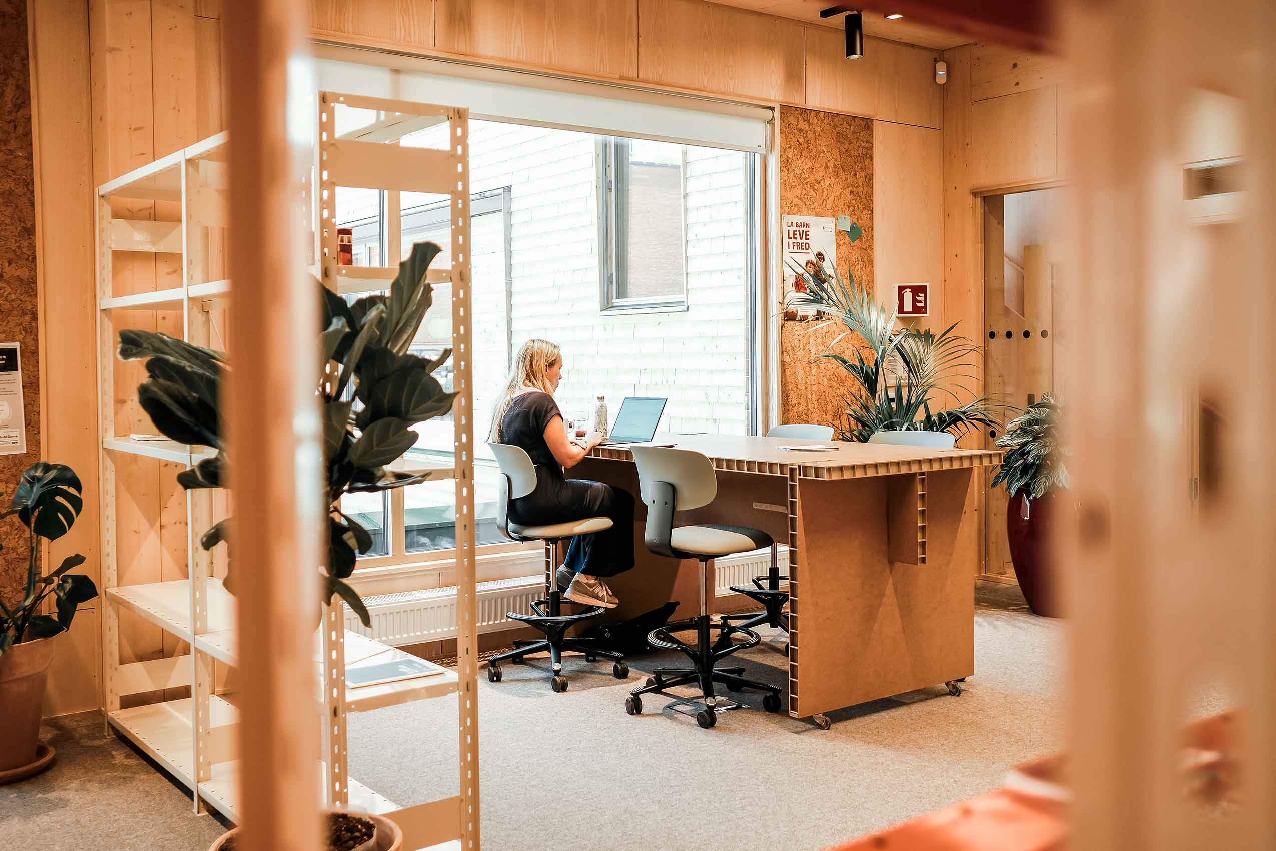 A lady looking at a laptop, sat on a HÅG Tion chair at a desk, with wooden walls and a plain carpet.