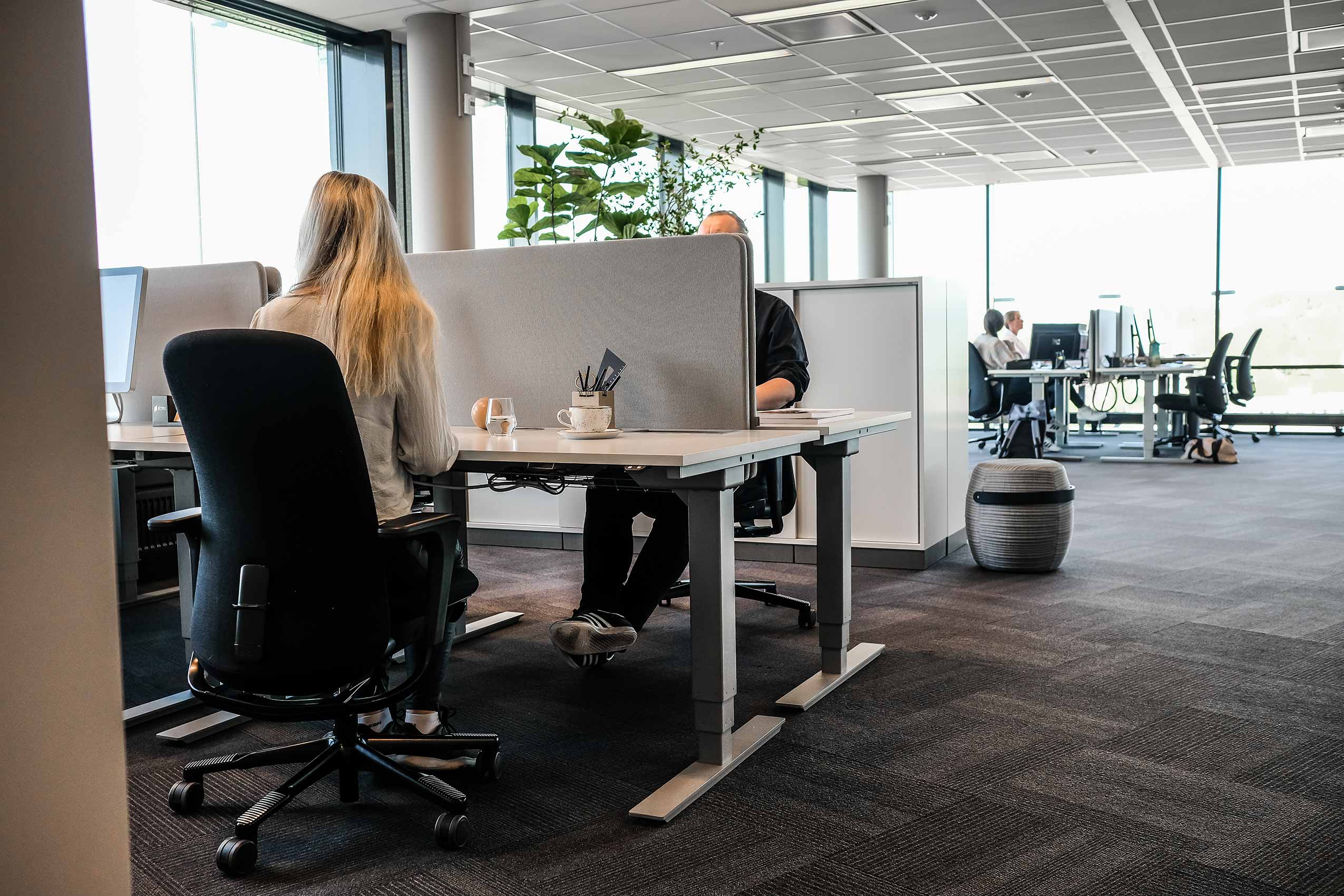 Two people sat in HÅG Sofi chairs opposite each other at workstatiosn in Strex's Oslo office